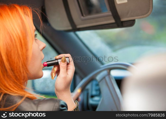 Concept of danger driving. Young woman driver red haired teenage girl painting her lips doing applying make up while driving the car.