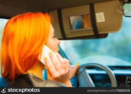 Concept of danger driving. Young woman driver redhaired girl talking on mobile phone smartphone while driving the car.