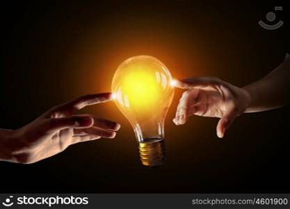 Concept of electric energy. Close up of human hands touching with finger light bulb