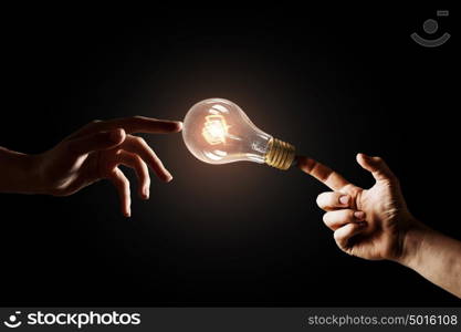 Concept of electric energy. Close up of human hands touching with finger light bulb