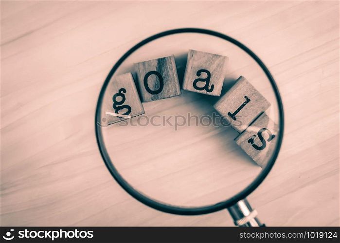 Concept of goals management, vintage and soft focus. Goals word typography cubes under magnifying glass over wooden texture backgroud, top view from above,