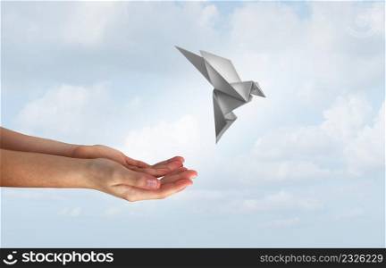Concept of hope and freedom as human hands release a magical flying origami bird made of paper as a liberty and democracy symbol for peace and love of humanity to stop war and spirituality passing icon.