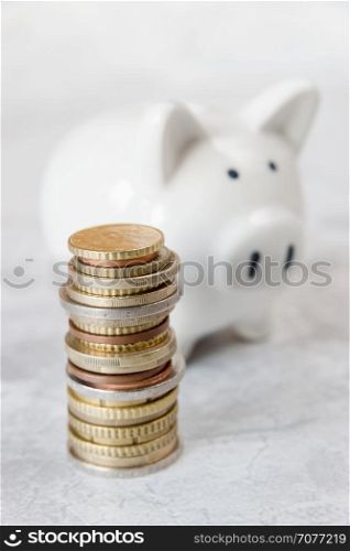 Concept of investing or saving: white ceramic piggy bank and a tower of euro coins