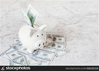 Concept of investing or saving: white ceramic piggy bank on the heap of dollars banknotes