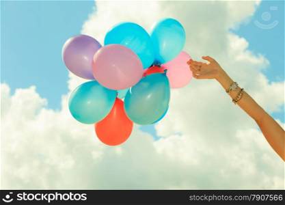 Concept of love in summer, freedom and wedding honeymoon. Female hand holding colorful balloons cloudy sky background, outdoor