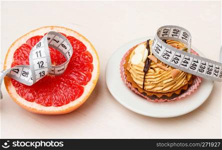 Concept of making choice: healthy low-calorie or unhealthy high-calorie food, slimming or fattening. Grapefruit and cake cupcake with measuring tape