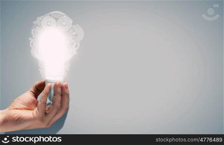 Concept of mechanism light bulb with gears inside in human hand. Light bulb with cogwheels