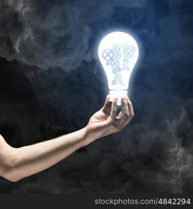 Concept of mechanism light bulb with gears inside in human hand. Light bulb with cogwheels