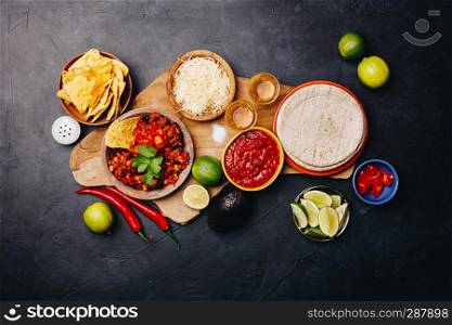 Concept of Mexican food corn tortillas, nachos, salsa, avocado, limes, cheese, chili con carne flat lay. Concept of Mexican food, flat lay, dark background