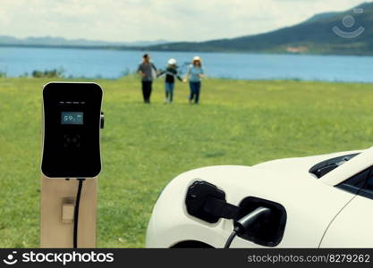 Concept of progressive happy family enjoying their time at green field and lake with electric vehicle. Electric vehicle driven by clean renewable from eco-friendly power sauce.. Concept of progressive happy family at green field, lake with electric vehicle.