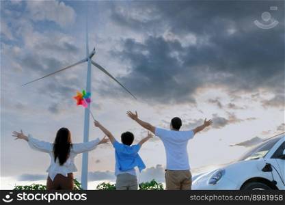 Concept of progressive happy family enjoying their time at wind farm with e≤ctric vehic≤. E≤ctric vehic≤driven by c≤an re≠wab≤e≠rgy from wind turbi≠≥≠rator for charging station.. Concept of progressive happy family at wind farm with e≤ctric vehic≤.