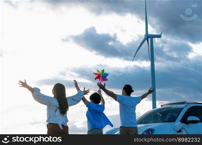 Concept of progressive happy family enjoying their time at wind farm with electric vehicle. Electric vehicle driven by clean renewable energy from wind turbine generator for charging station.. Concept of progressive happy family at wind farm with electric vehicle.