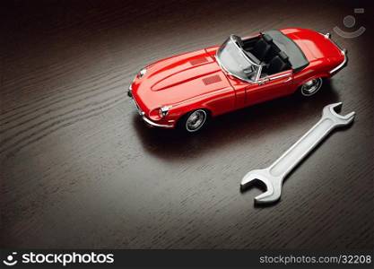Concept of repair, maintenance and servicing of machines. Model of red cabriolet and wrench on wooden surface. Copy space
