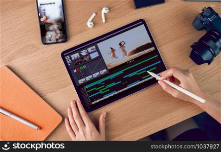 Concept of simple operation of blogger and vlogger, hand using digital pen on video editor works with footage on tablet, camera and accessories on table.