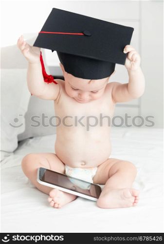 Concept of smart baby. Cute baby boy in graduation cap browsing internet on digital tablet