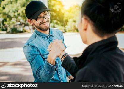 Concept of two friends greeting each other and shaking hands on the street. Two teenage friends shaking hands at each other outdoors. Two people shaking hands on the street