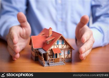 concept with model of house and hands of man, selective focus on nearest part of small building