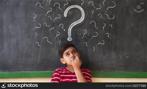 Concepts on blackboard at school. Young people, quiet student and pupil in classroom. Hispanic boy with doubts and thoughts in class. Portrait of male child thinking