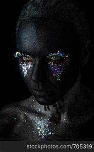 Conceptual art Portrait of Beautiful Woman in Black makeup with Sparkles on a Face isolated on a dark background. Girl in black makeup with sparkles