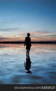 Conceptual image of young boy walking on water in sunset landscape