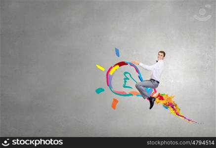 Conceptual image of young businessman riding light bulb. Master of creativity