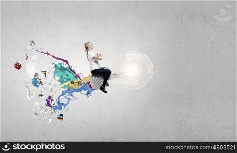 Conceptual image of young businesswoman riding light bulb. Master of creativity