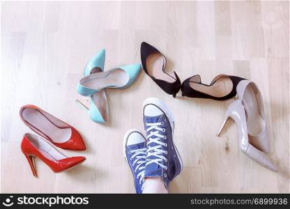 Conceptual image with a girl&rsquo;s feet wearing sneakers, while surrounded by elegant, high heels shoes. Choosing comfort over elegance.