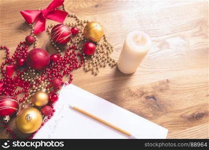 Conceptual image with a letter addressed to Santa, on a wooden table, surrounded by Christmas decorations and a lit candle.