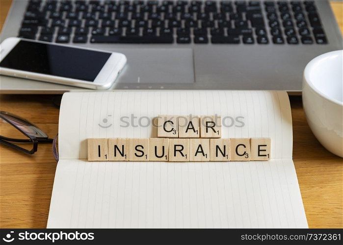 Conceptual keyword car insurance in wooden tile letters in personal home desk setting with laptop, notebook and accessories