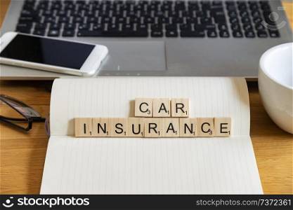 Conceptual keyword car insurance in wooden tile letters in personal home desk setting with laptop, notebook and accessories