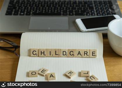 Conceptual keyword childcare in wooden tile letters in wooden tile letters in personal home desk setting with laptop, notebook and accessories