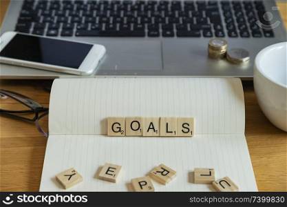 Conceptual keyword goals  in wooden tile letters in personal home desk setting with laptop, notebook and accessories