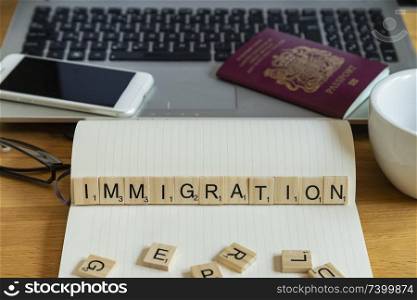 Conceptual keyword immigration in wooden tile letters  in personal home desk setting with laptop, notebook and accessories