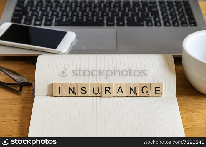 Conceptual keyword in wooden tile letters insurance in personal home desk setting with laptop, notebook and accessories