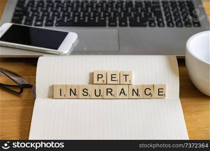 Conceptual keyword in wooden tile letters  pet insurance in personal home desk setting with laptop, notebook and accessories