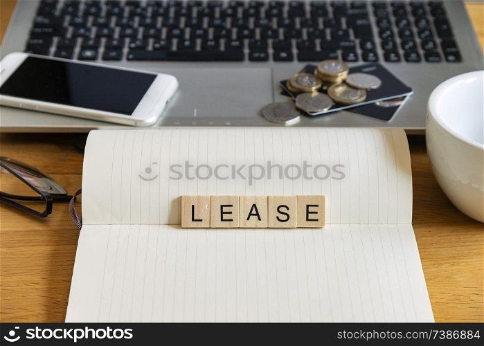 Conceptual keyword lease in generic wooden tile letters  in personal home desk setting with laptop, notebook and accessories