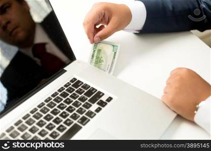 Conceptual photo of businessman receiving digital money transfer. Man pulling dollar bill out of laptop