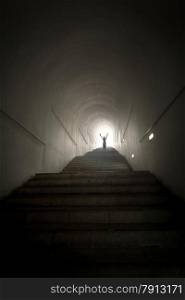 Conceptual photo of person standing in the end of tunnel at light beam with hands raised