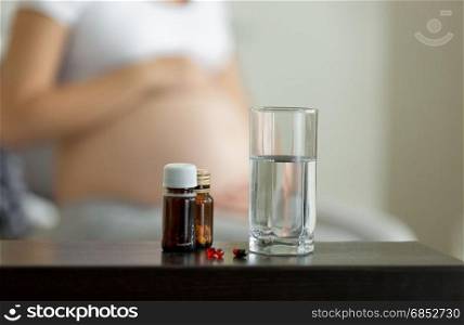 Conceptual photo of pregnancy healthcare. Medicines on table next to pregnant woman