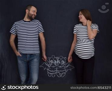 Conceptual photo of pregnant couple drawing their imaginations about the future life with children on chalk board. pregnant couple drawing their imaginations on chalk board