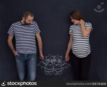 Conceptual photo of pregnant couple drawing their imaginations about the future life with children on chalk board. pregnant couple drawing their imaginations on chalk board