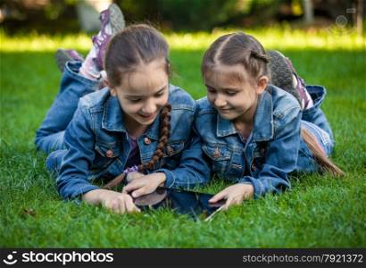 Conceptual photo of two twin girls using tablet at park