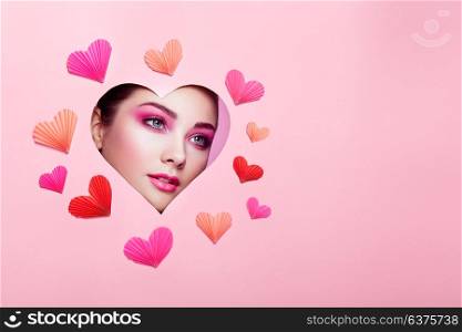 Conceptual photo of Valentine&rsquo;s day. Face of Girl with Festive Pink Makeup. Paper hearts on a pink background. Love symbols Valentines day