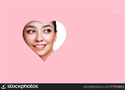 Conceptual photo of Valentine&rsquo;s day. Face of Girl with Festive Pink Makeup. Paper hearts on a pink background. Love symbols Valentines day