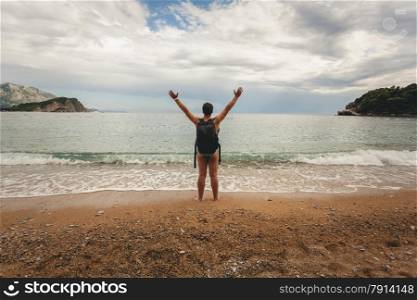 Conceptual photo of young man wearing backpack stretching out hands on sea beach