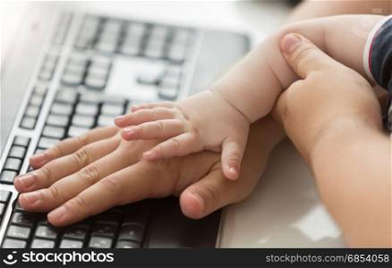 Conceptual shot of adult and baby hands on computer keyboard
