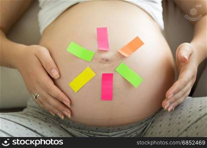 Conceptual shot of pregnant woman with colorful memo stickers on big belly