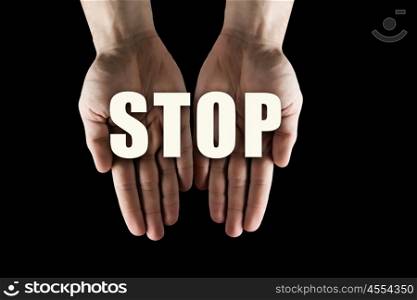 Conceptual word in palms. Male hands on dark background showing in palms word stop