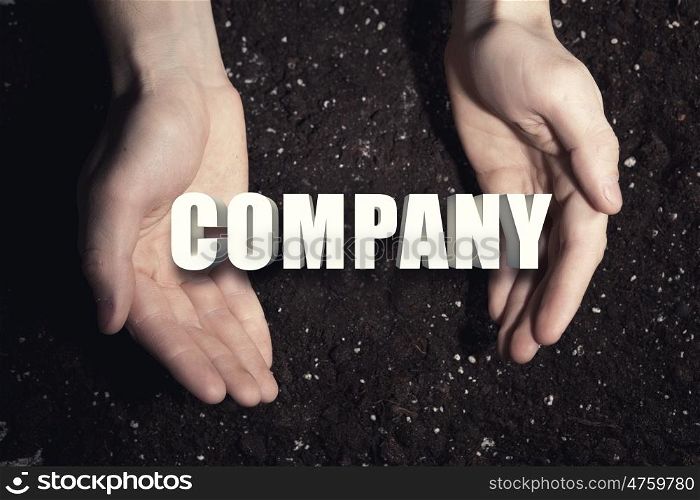Conceptual word in palms. Male hands on soil background showing in palms idea word company
