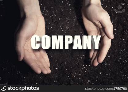 Conceptual word in palms. Male hands on soil background showing in palms idea word company